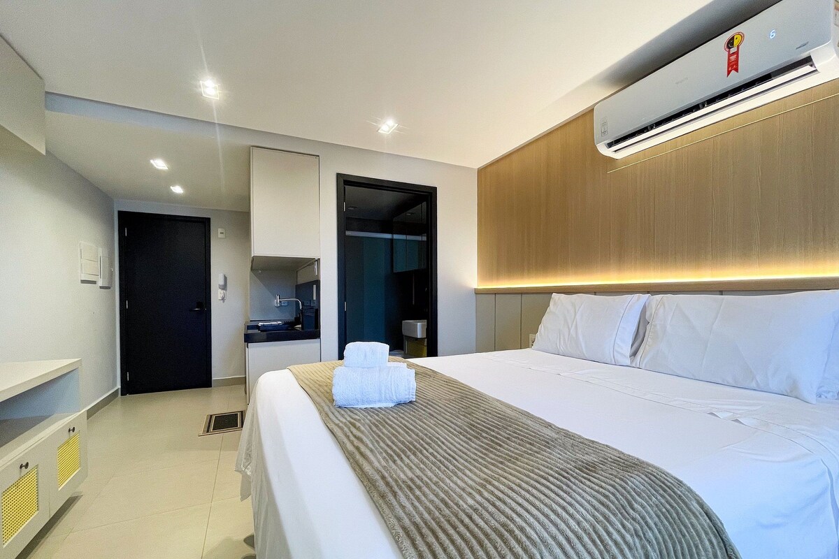 Quarto de hotel com cama, banheiro, escrivaninha e ar condicionado.