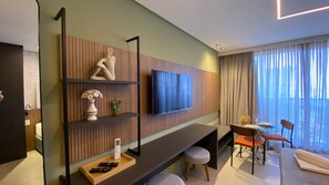 A modern hotel room with a flat-screen TV mounted on the wall, a dining area with a table and chairs, and a large window with curtains. - Way by Hosppedar (João Pessoa)