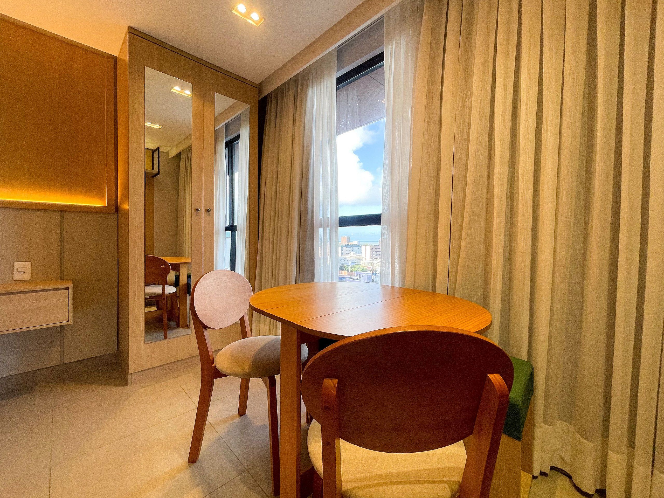 Camera d'albergo con zona pranzo, vista sulla città e un'ampia finestra con tende.
