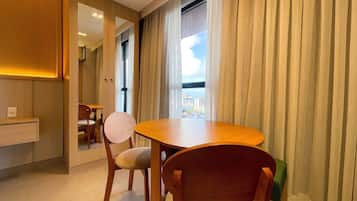 Camera d'albergo con zona pranzo, vista sulla città e un'ampia finestra con tende.