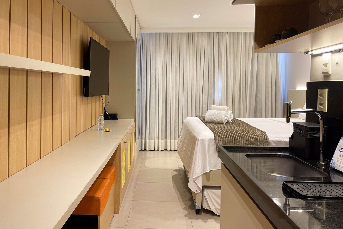 Quarto de hotel moderno com uma cama, televisão fixada na parede, pia e bancada.