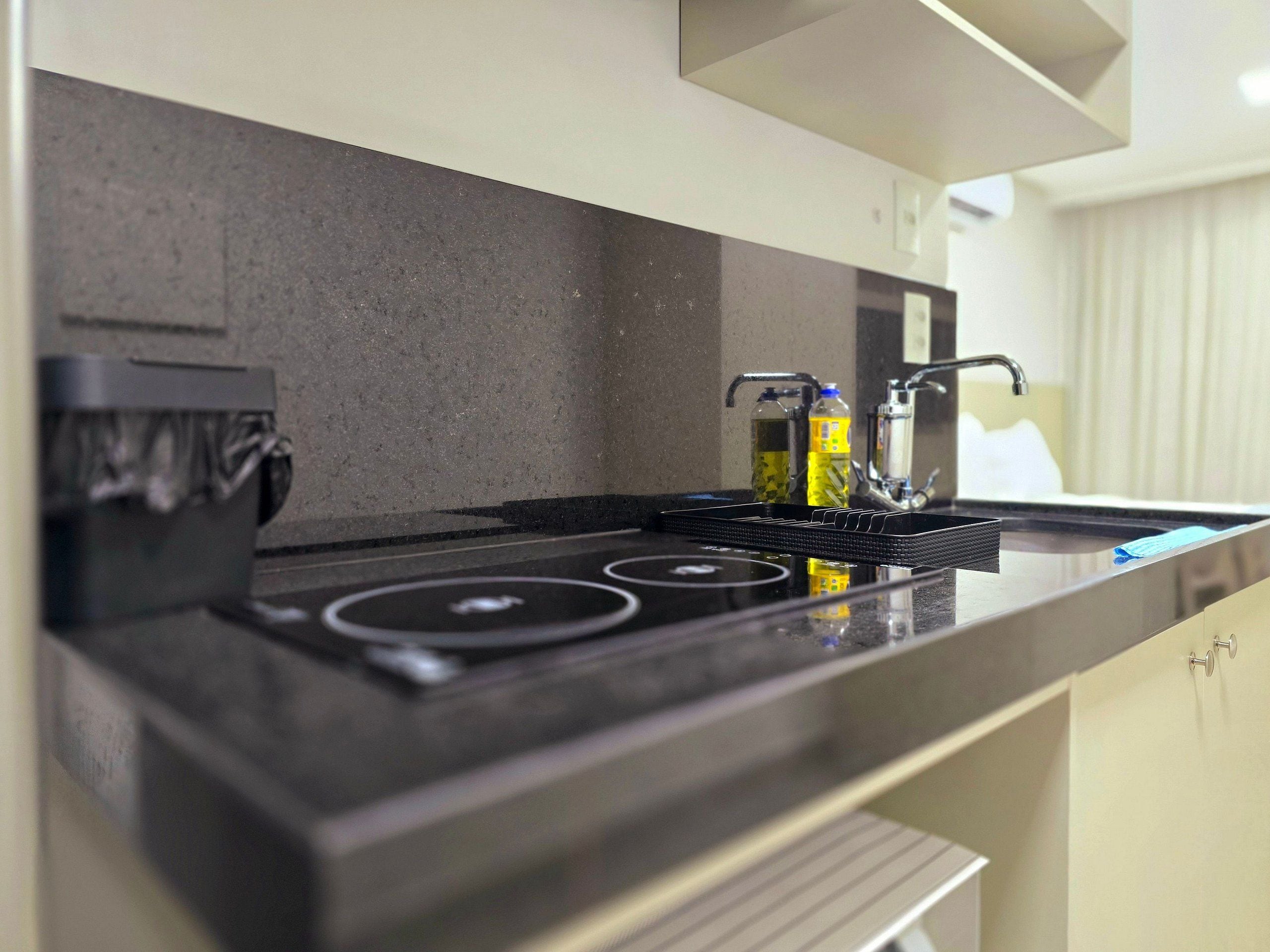 Uma cozinha moderna com bancada preta, eletrodomésticos de aço inoxidável e forno embutido.