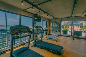 Un gimnasio con cintas de correr, una bicicleta estática y amplias ventanas con vistas a la ciudad.