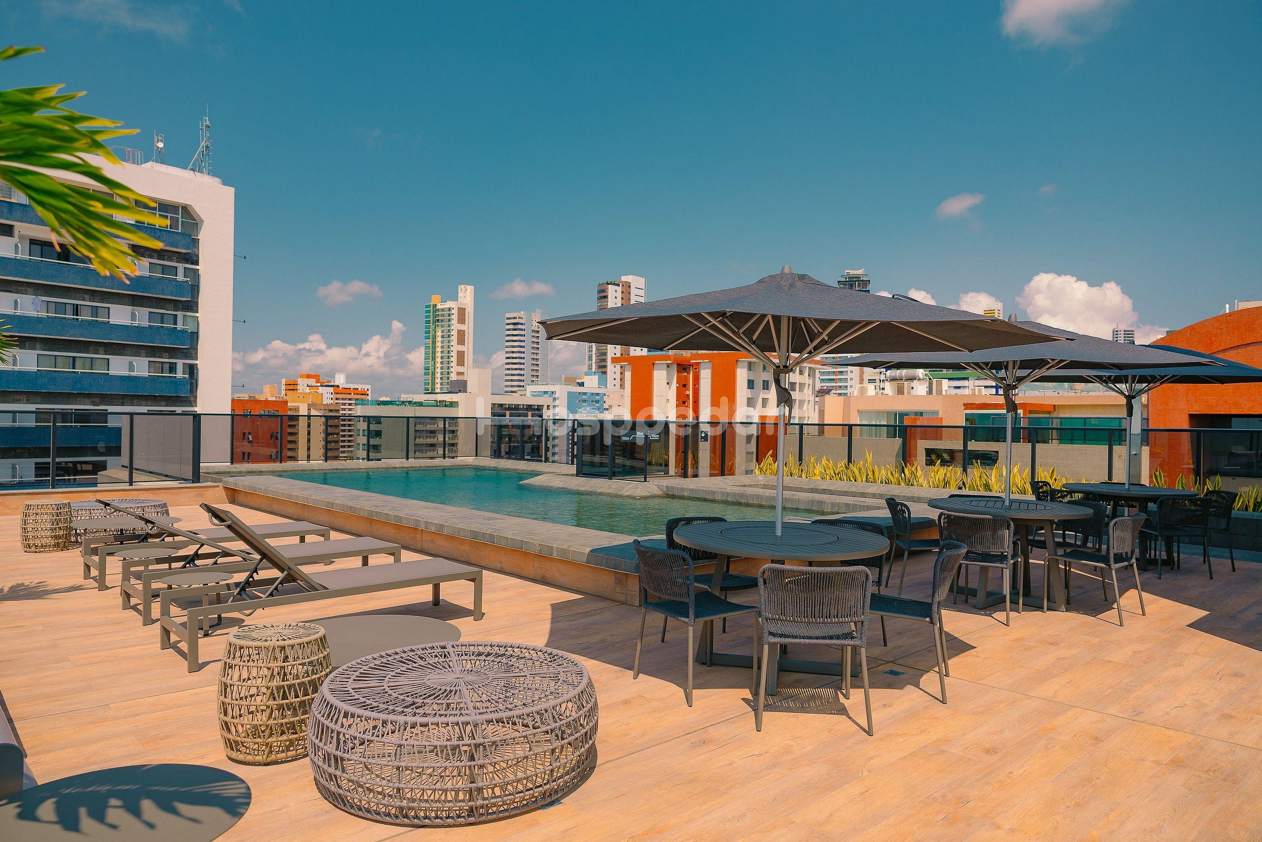 A rooftop pool area with lounge chairs, tables, and umbrellas.