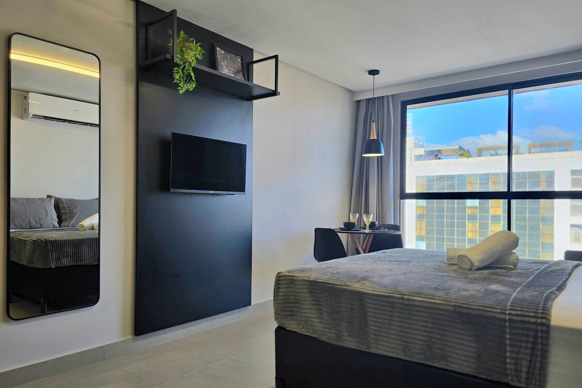 Quarto de hotel moderno com cama, TV de tela plana, janela grande e vista para a cidade.