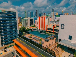 Um edifício alto com piscina no terraço, várias varandas e vista para o horizonte da cidade.