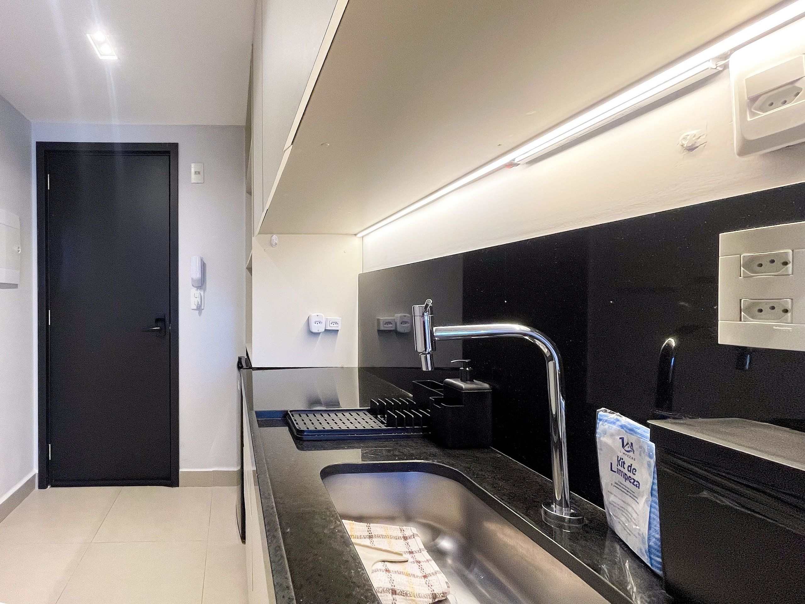 Una cucina moderna con lavello in acciaio inox, piano di lavoro nero e una porta nera.