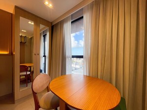 Um quarto com uma mesa de madeira redonda, duas cadeiras, um espelho e vista para a cidade através de uma janela com cortinas.