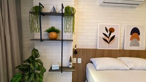 A modern bedroom with a bed, a nightstand, a shelf with plants, and two abstract wall art pieces. - Way by Hosppedar (João Pessoa)