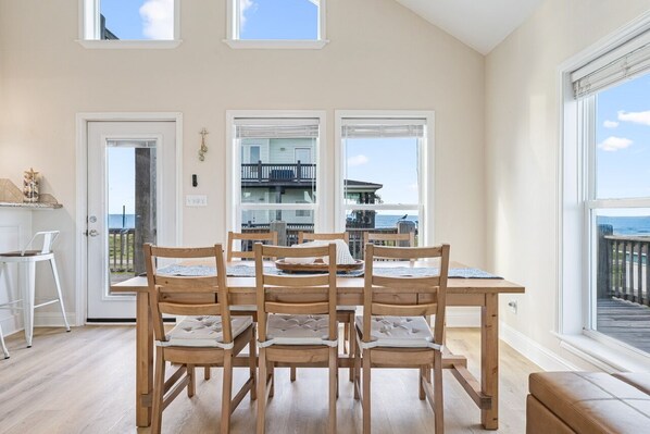 A dining area with a wooden table and chairs, a view of the sea through large windows, and a balcony with a railing. - 2nd Row with incredible gulf views, fenced yard, seconds to the beach! (Crystal Beacg)