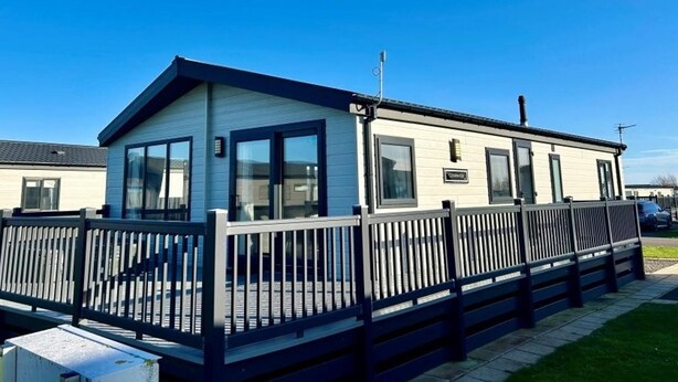 A mobile home with a fenced deck, large windows, and a sign indicating 'Cottages.' - Luxury Lodge Sleeps 6 With Hot Tub and Parking (Mablethorpe)