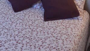 A bed with floral bedding and two dark pillows, a window with a view of the interior, and a wall-mounted light fixture. - Charming one-bedroom apartment for a couple, near the beaches of Capbreton, (Capbreton)