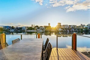 Un pontile in legno con tavolo e sedie che si affaccia su un corpo d'acqua tranquillo, con edifici sullo sfondo.