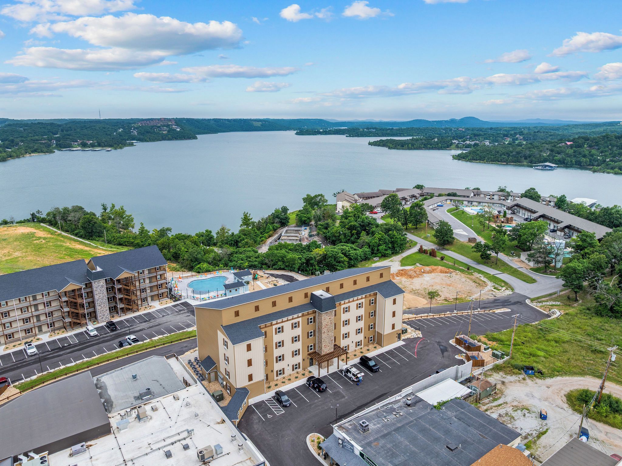 Ein mehrstöckiges Hotel mit Schwimmbad, Parkplatz und Blick auf einen großen See.