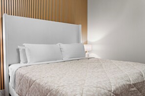 En säng med ett mönstrat överkast och två kuddar, ett sängbord med en lampa och en väggpanel av träribbor.