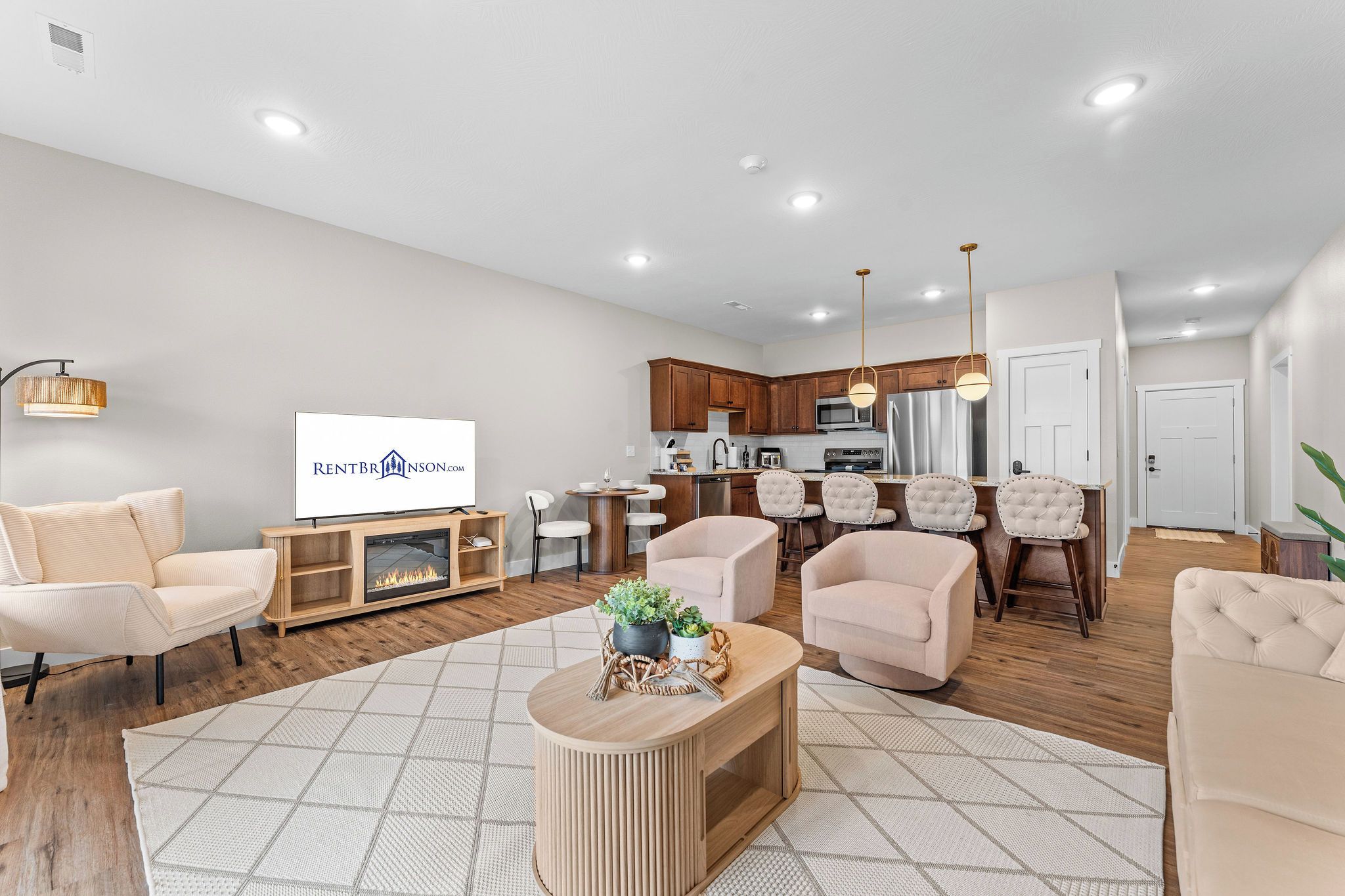 A modern living room with a fireplace, a dining area with a kitchen in the background, and a television displaying a logo.