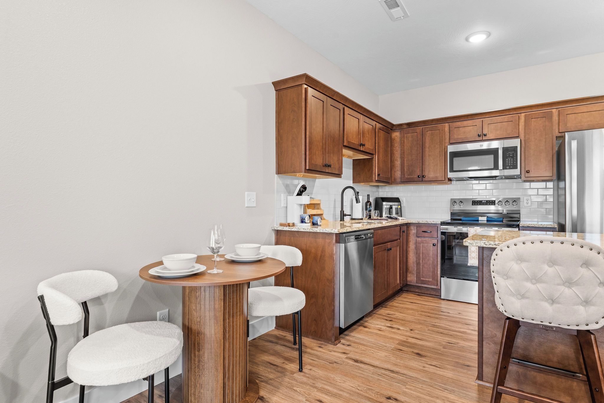 A modern kitchen with wooden cabinets, stainless steel appliances, and a round dining table with white chairs.