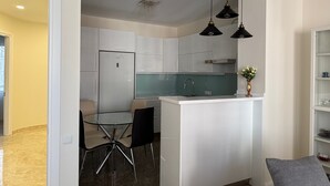 A modern kitchen with white cabinetry, a glass dining table, and black pendant lights. - Bright Modern 2BR Apt near Central Park & Beach (Batumi)