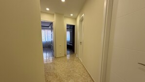 A hallway with marble flooring, white walls, and doors leading to other rooms. - Bright Modern 2BR Apt near Central Park & Beach (Batumi)