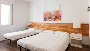 Ein Hotelzimmer mit zwei Einzelbetten, einem Holzkopfteil, einem Stadtbildgemälde, einem Fenster und einem Nachttisch mit Lampe.