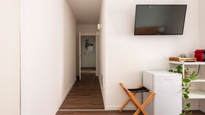 Ein Flur mit Holzboden, einem weißen Kühlschrank, einem an der Wand montierten Fernseher und einem kleinen Tisch mit einem roten Gegenstand darauf.