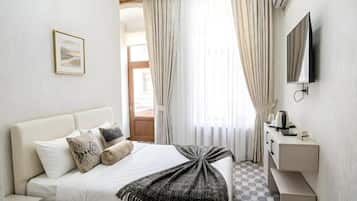 Quarto de hotel com cama, mesa de cabeceira com chaleira, televisão e vista para o exterior.
