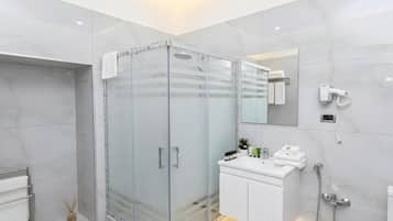 Casa de banho moderna com chuveiro em cabine de vidro, toucador branco com espelho e secador de cabelo fixado na parede.
