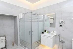A modern bathroom with a glass-enclosed shower, a white vanity with a mirror, and a hairdryer mounted on the wall. - Epicenter Hotel Baku (Baku)