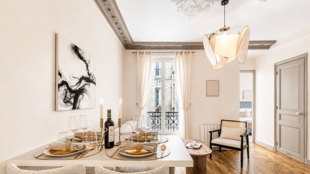A dining area with a table set for four, a chandelier, and a view of the city through a window. - 1518 Trétaigne (Paris)