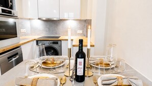 A modern kitchen with a dining area set for a meal, featuring a wine bottle, candles, and a clean, minimalist design. - 1518 Trétaigne (Paris)