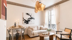 A modern living room with a sofa, coffee table, and dining table set with candles and plates. - 1518 Trétaigne (Paris)