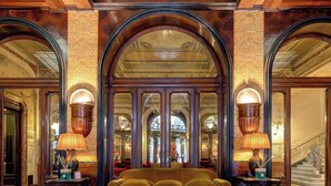 A luxurious lobby with a central sofa, ornate columns, and a marble floor.
