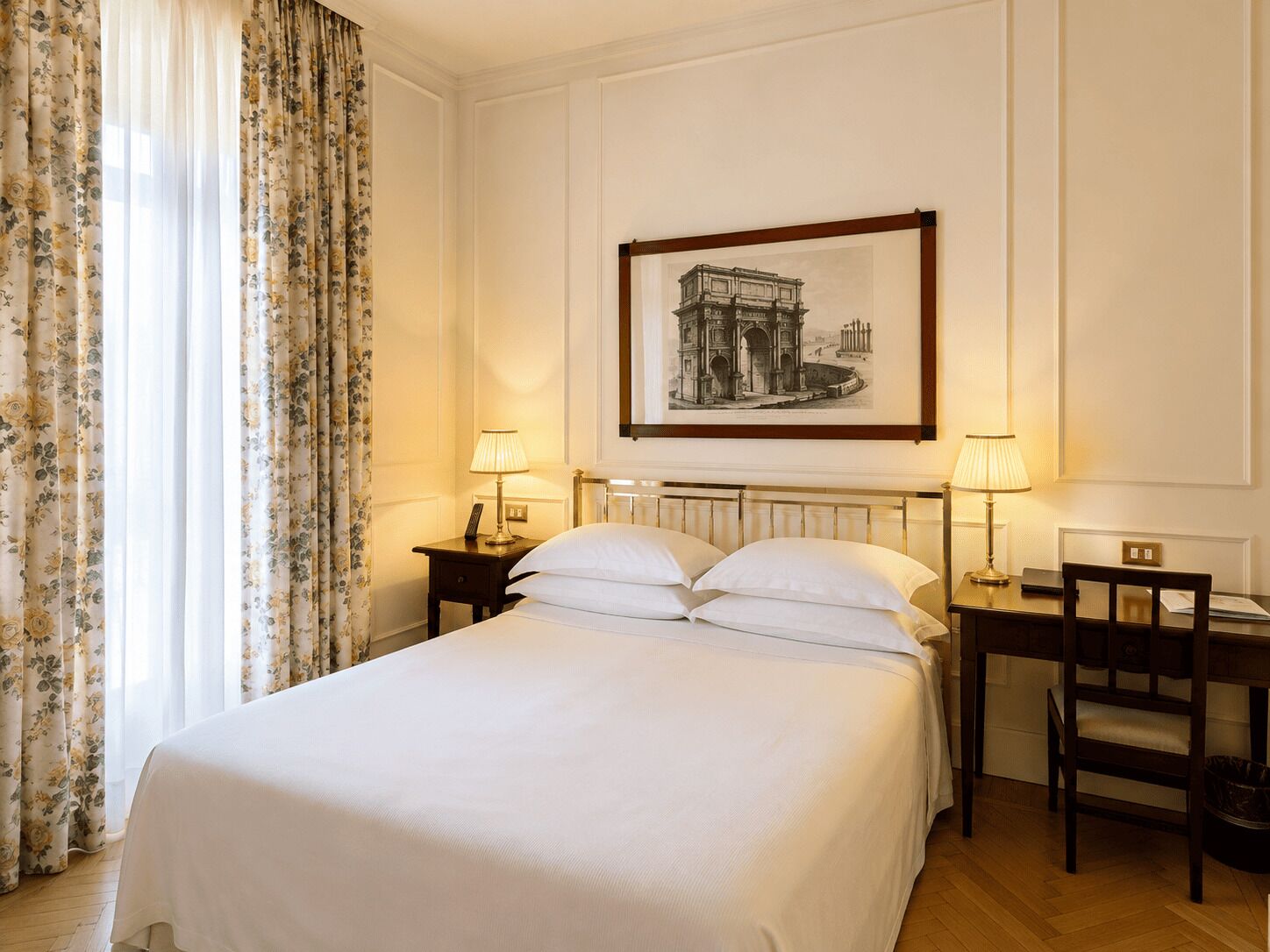 Une chambre d’hôtel avec un lit, deux tables de chevet avec des lampes, une chaise et un tableau encadré au mur.