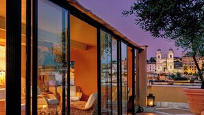 A glass-enclosed patio with wicker furniture, a tiled floor, and a view of a cityscape at dusk.