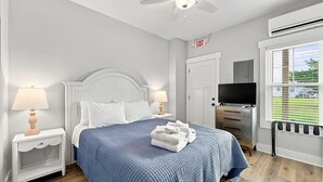 A bedroom with a bed, two bedside tables with lamps, a television, and a window with blinds. - Circle Pearl-Ocean View Townhome (Atlantic Beach)