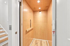 Ein Aufzuginnenraum aus Holz mit Bedienfeld, Warnschild und Holzboden.