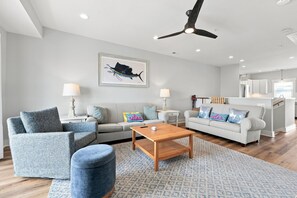 Ein modernes Wohnzimmer mit einer Couch, Sesseln, einem Couchtisch und einem Deckenventilator.
