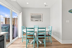 A dining area with a white table and turquoise chairs, a large window with a view of a wooden deck, and a mirror on the wall. - Circle Pearl-Ocean View Townhome (Atlantic Beach)