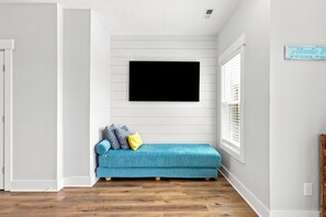 Ein Zimmer mit blauem Sofa, einem flachbildfernseher an der Wand und einem Fenster mit Jalousien.
