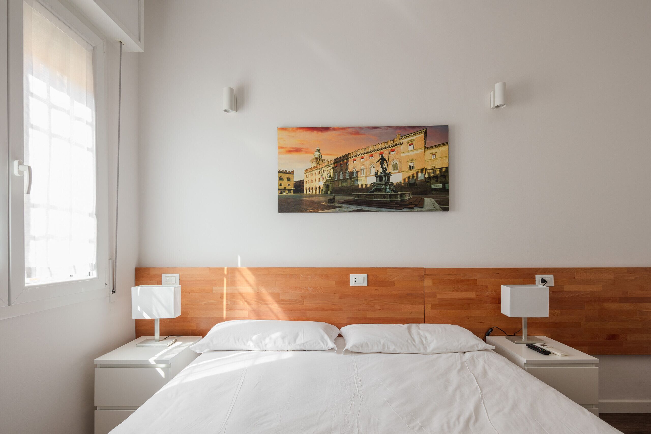 Een hotelkamer met een bed, twee nachtkastjes, een aan de muur hangend schilderij en een raam.