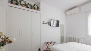A bedroom with a bed, a TV, a radiator, a wardrobe, and a small table with a chair. - Manzoni Room by Wonderful Italy (Bologna)