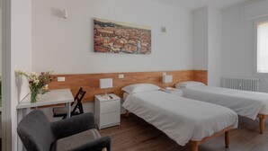 Ein Hotelzimmer mit zwei Betten, einem Schreibtisch, einem Stuhl, einem Nachttisch, einer Lampe und einem Bild an der Wand.