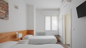 Ein Hotelzimmer mit zwei Betten, einem Heizkörper, einem Fenster und einem Fernseher.
