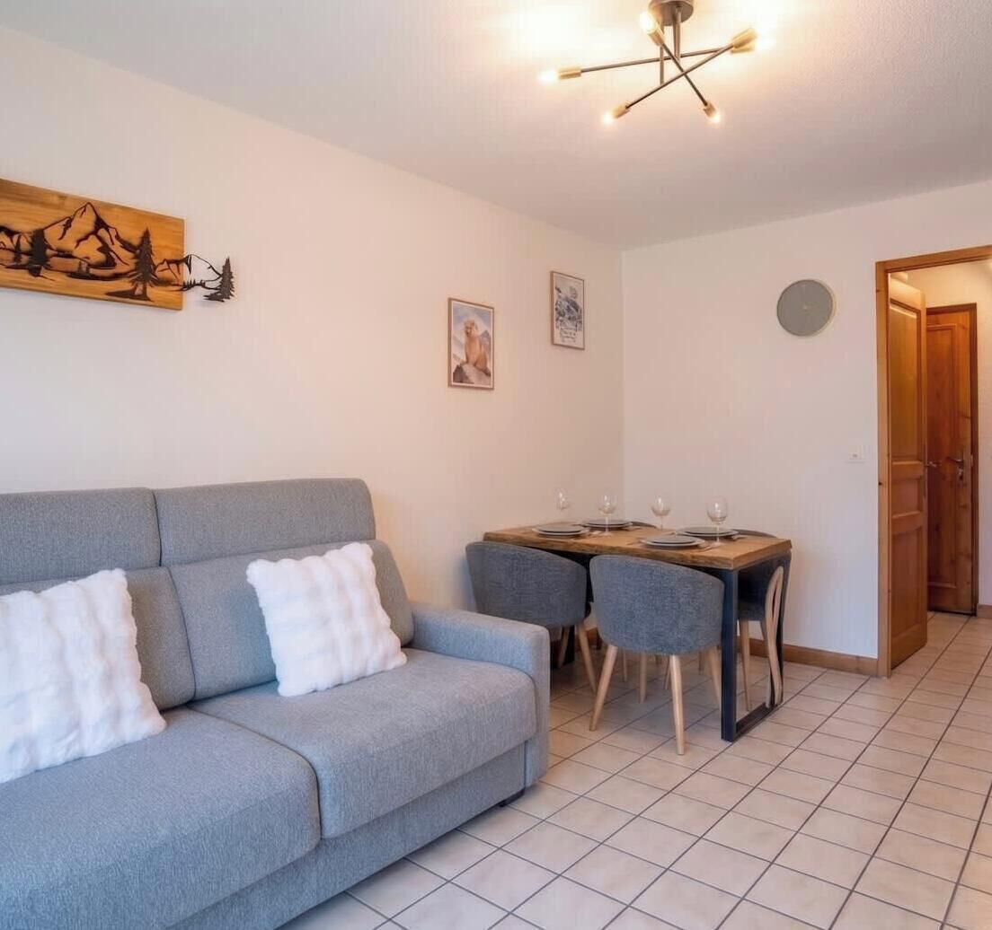 Un salon avec un canapé gris, une table à manger en bois avec des chaises, une œuvre d’art accrochée au mur et un luminaire suspendu au plafond.