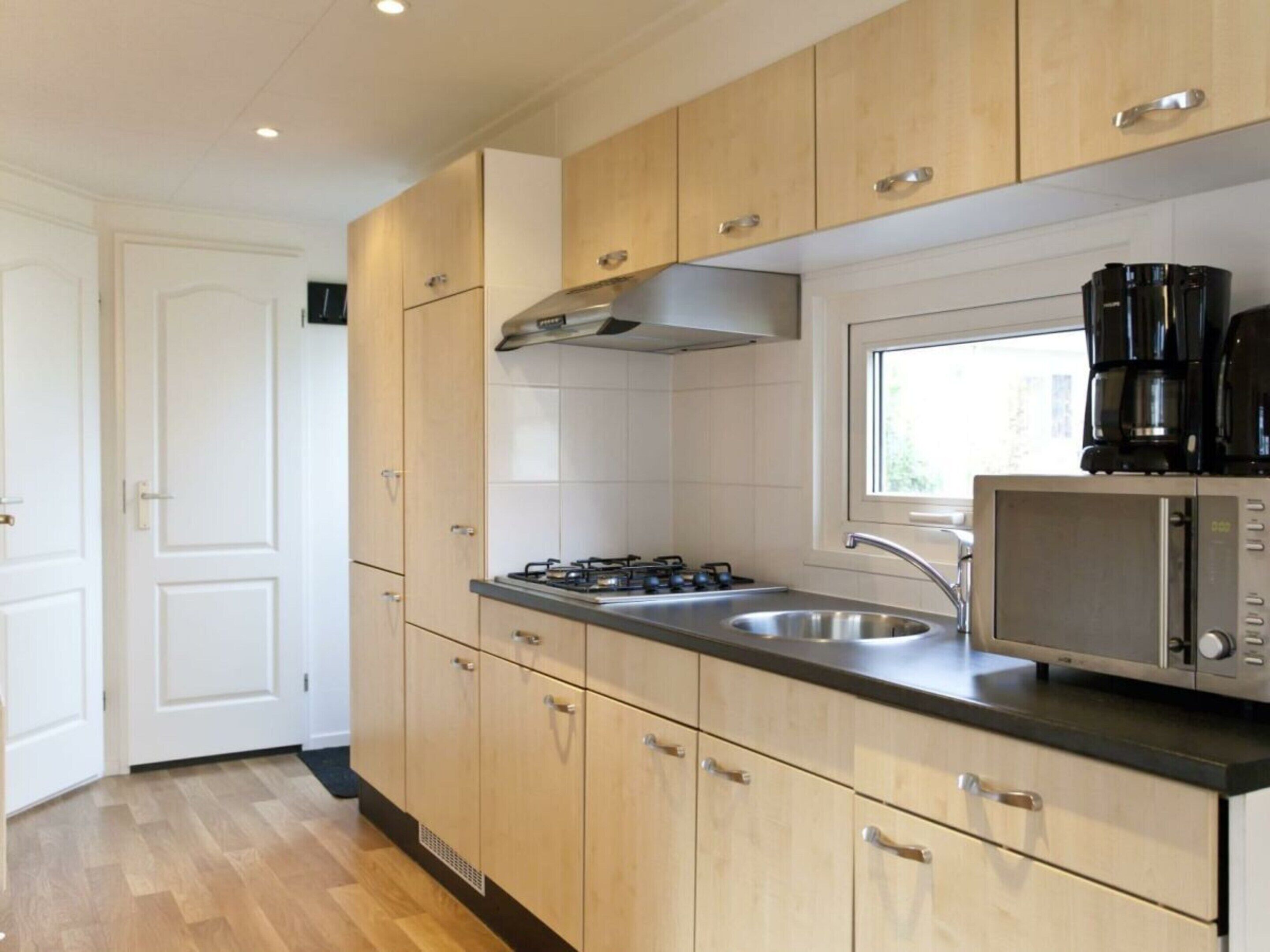 A modern kitchen with wooden cabinets, a stainless steel sink, a gas stove, a microwave, and a coffee maker.