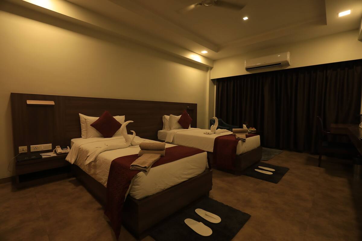 A hotel room with two beds, a desk, and an air conditioning unit.
