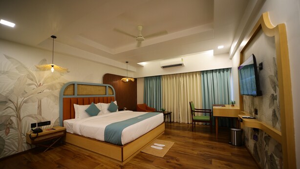 A hotel room with a wooden bed, a desk, a chair, a ceiling fan, an air conditioning unit, and a television on the wall.
