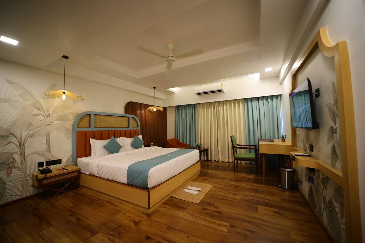 A hotel room with a wooden bed, a desk, a chair, a ceiling fan, an air conditioning unit, and a television on the wall.