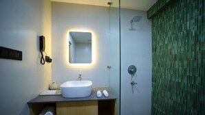 A modern bathroom with a white sink, a mirror with a light, a shower, and a towel rack.