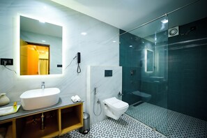 A modern bathroom with a large mirror, a white sink, a toilet, and a glass-enclosed shower area. - Surya Garden (Talcher)